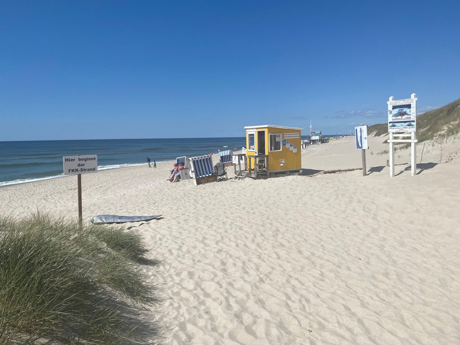 Sign marking the start of a designated FKK beach at Hörnum on Sylt, Germany, beside dunes and the sea.